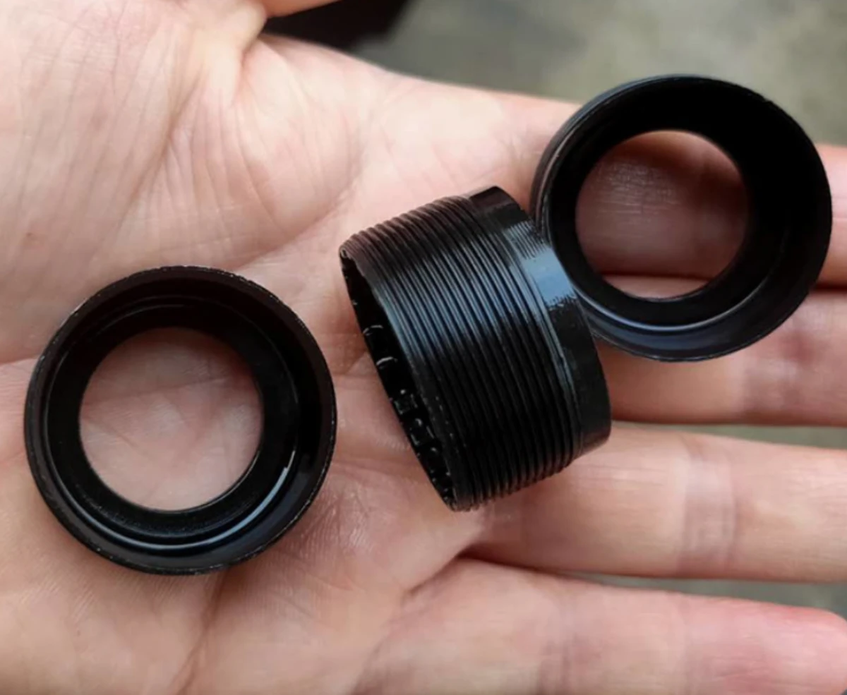 Machined steel parts with a black oxide finish, held in a hand, showing fine threads and a deep black surface