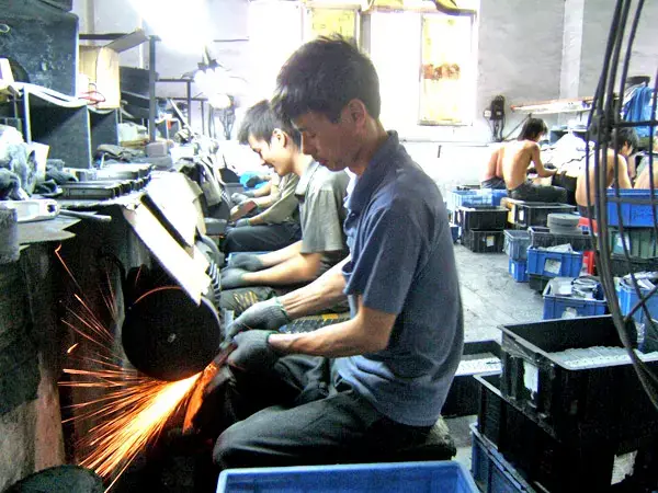 Worker hand-polishing metal parts on a bench grinder in the finishing workshop GY Machining uses