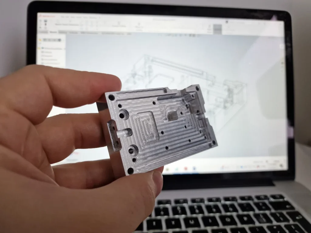 Milled aluminium prototype plate held in front of the CAD model it was machined from