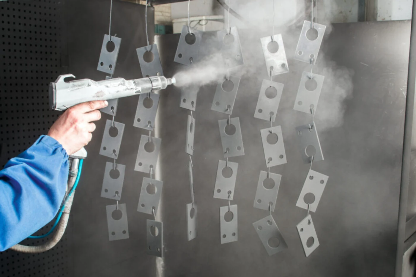 Operator spraying powder coating onto machined parts hung in a spray booth