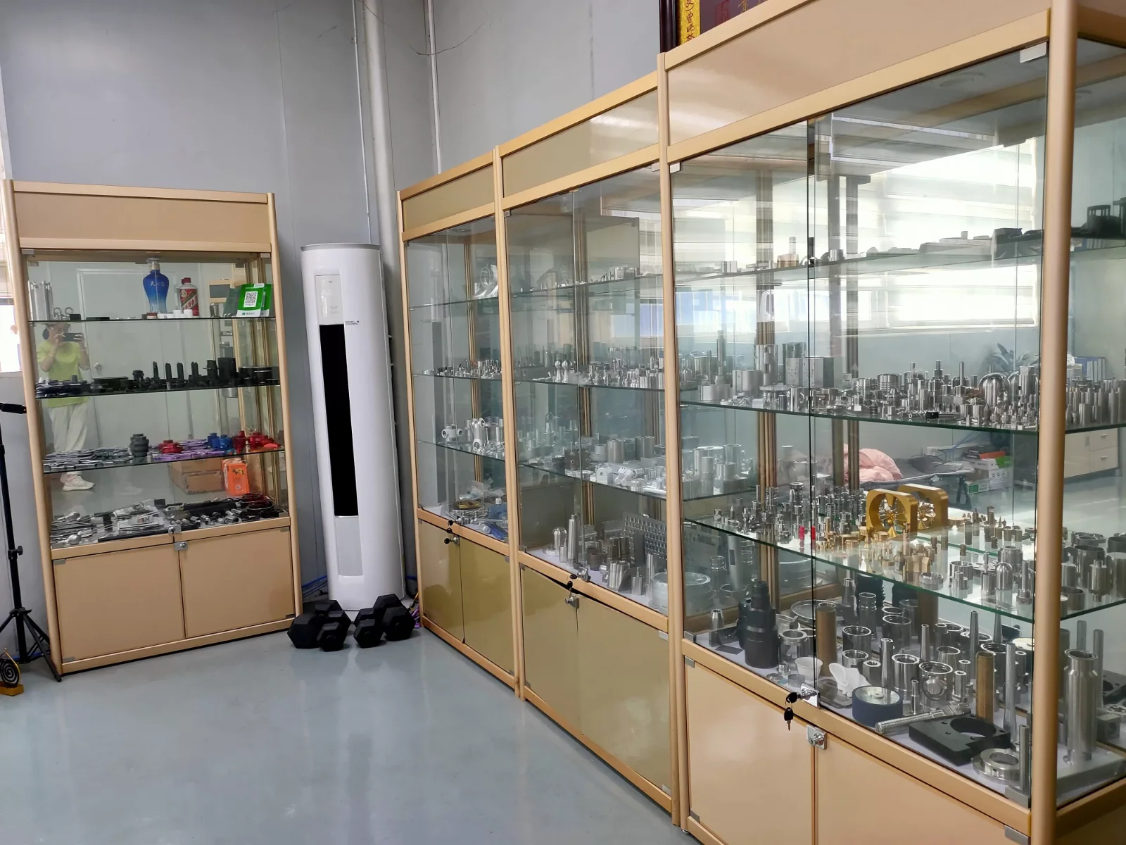 Sample room at GY Machining in Dalingshan, Dongguan: four display cabinets of retained CNC machined parts in stainless steel, aluminium and brass