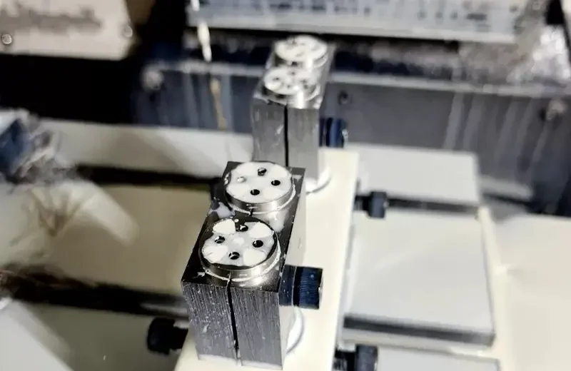 Turned stainless steel thumb screws held in a vise for second-operation milling of the head hole pattern at GY Machining